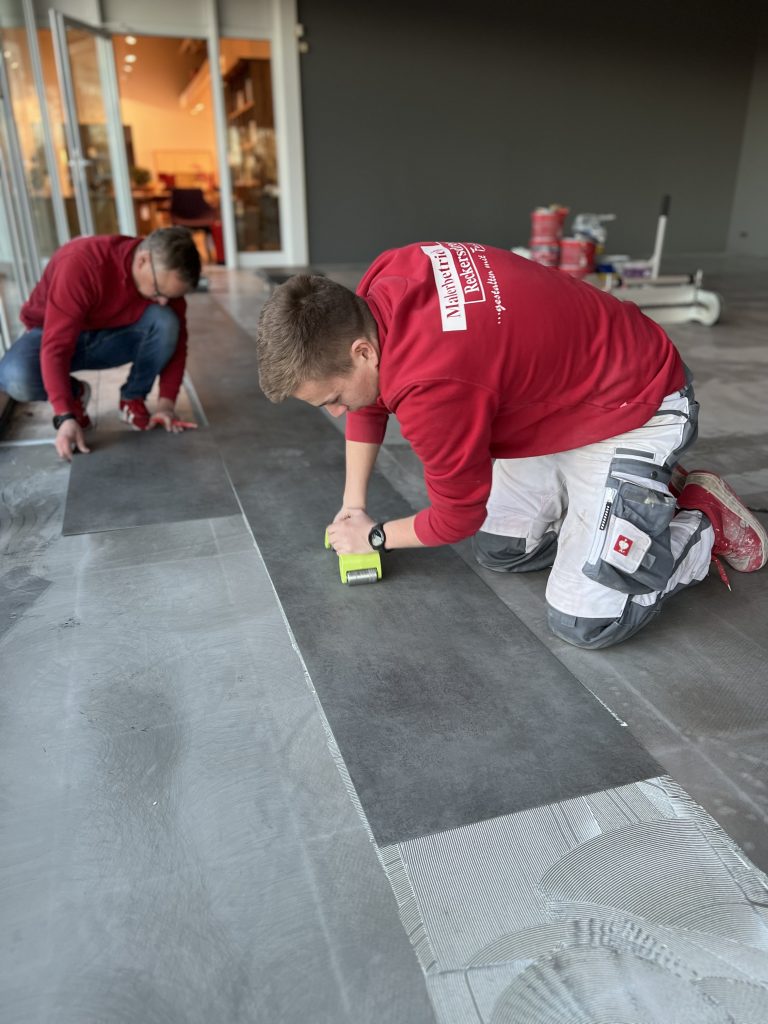 André und Max Reckersdrees verlegen großformatige Bodenplatten und drücken die Fugen mit einer Andruckrolle an